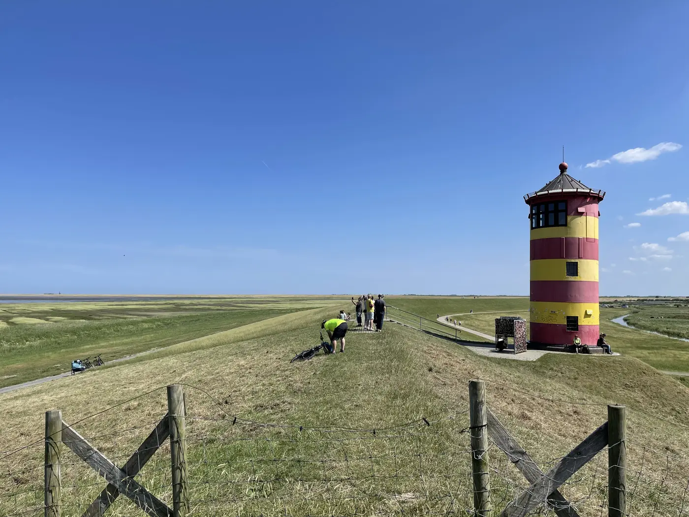 Der Pilsumer Leuchtturm aus der Nähe, davor ein Weidezaun auf dem Deich