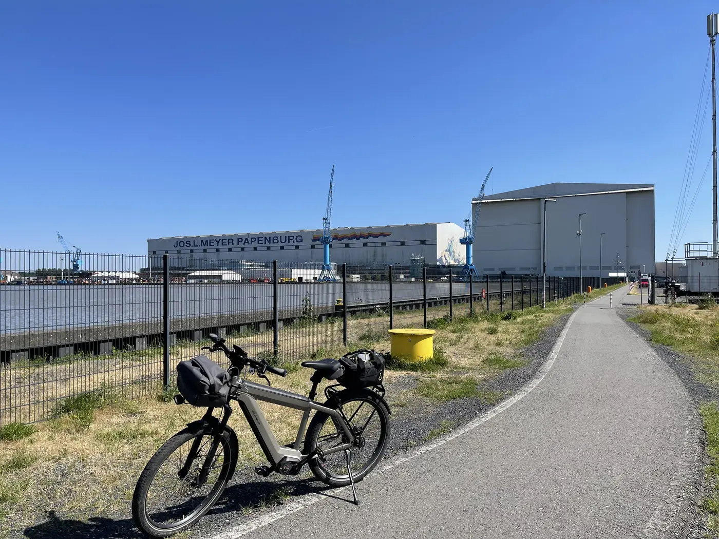 Das Rad am Radweg bei Papenburg, dahinter die hellen Hallen der Werft